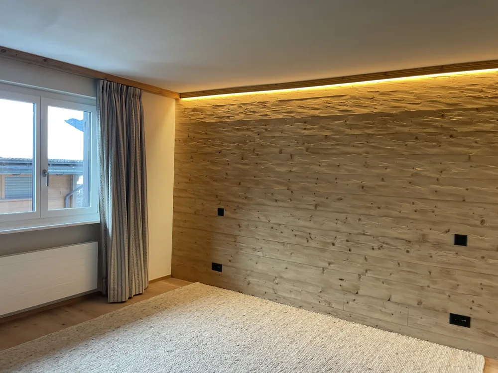 Finished chalet bedroom lined in reclaimed timber with a concealed light cove and window onto snow
