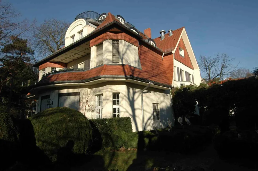 Turn-of-the-century Berlin villa with red tiled roof, rounded corner tower and hedged garden